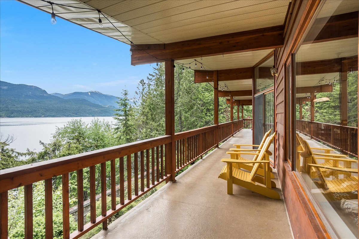 Covered deck with yellow Adirondack chairs and panoramic views over Kootenay Lake to the mountains